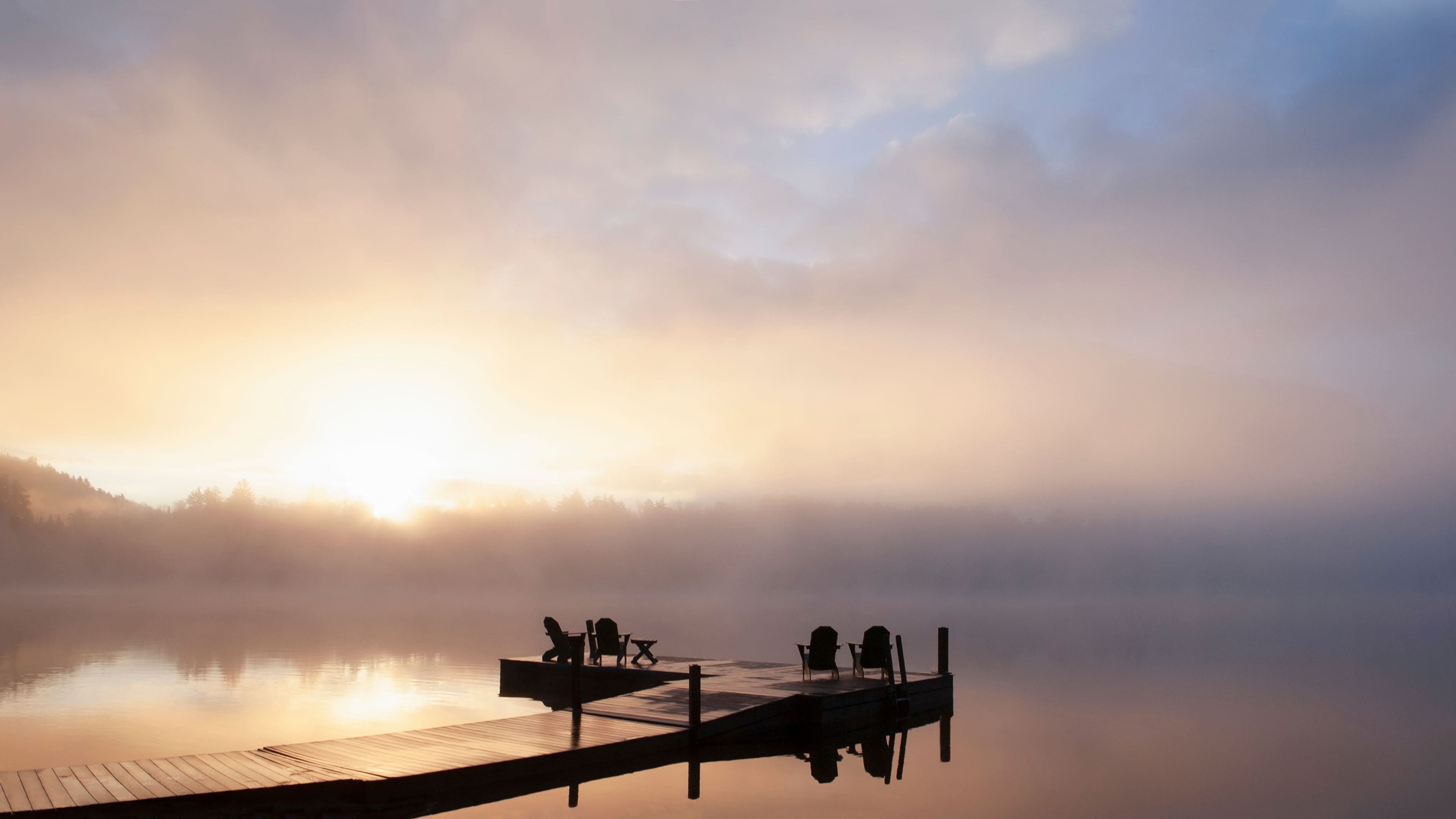 Silhouettes of adirondack chairs on pier on Lake Placid at sunrise