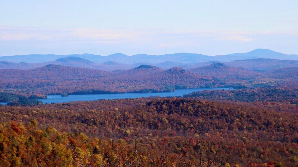 A mountainous landscape with a lake surrounded by autumn-colored forests.