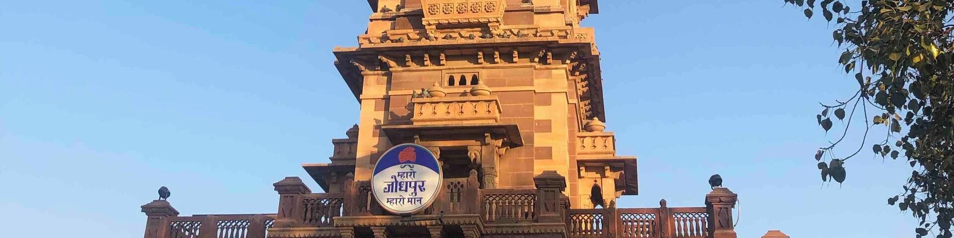 A tall clock tower with intricate carvings and a sign in a local language.