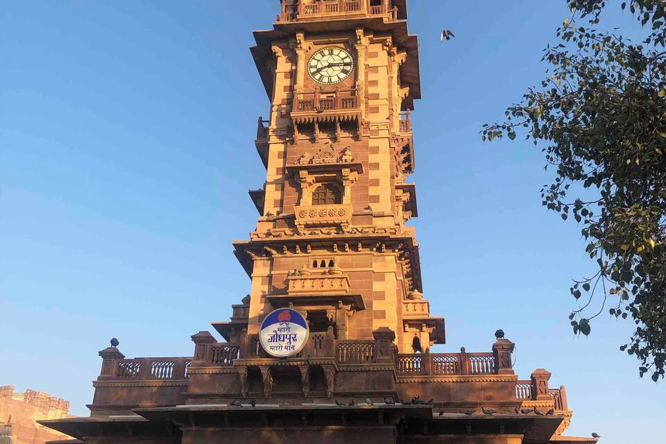 A tall clock tower with intricate carvings and a sign in a local language.