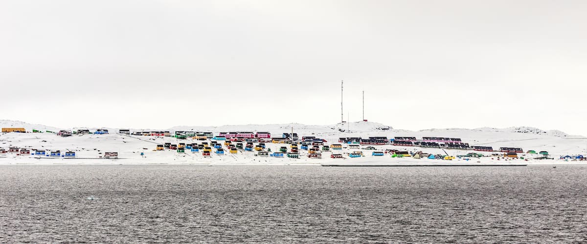 A snowy landscape with colorful buildings and a large body of water.