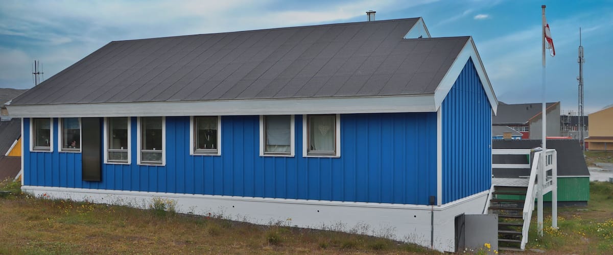 A small blue house with a grey roof, white trim, and a flagpole with a flag.