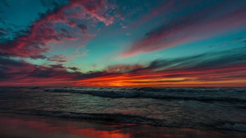 A sunset over the ocean with waves and a sky filled with clouds.