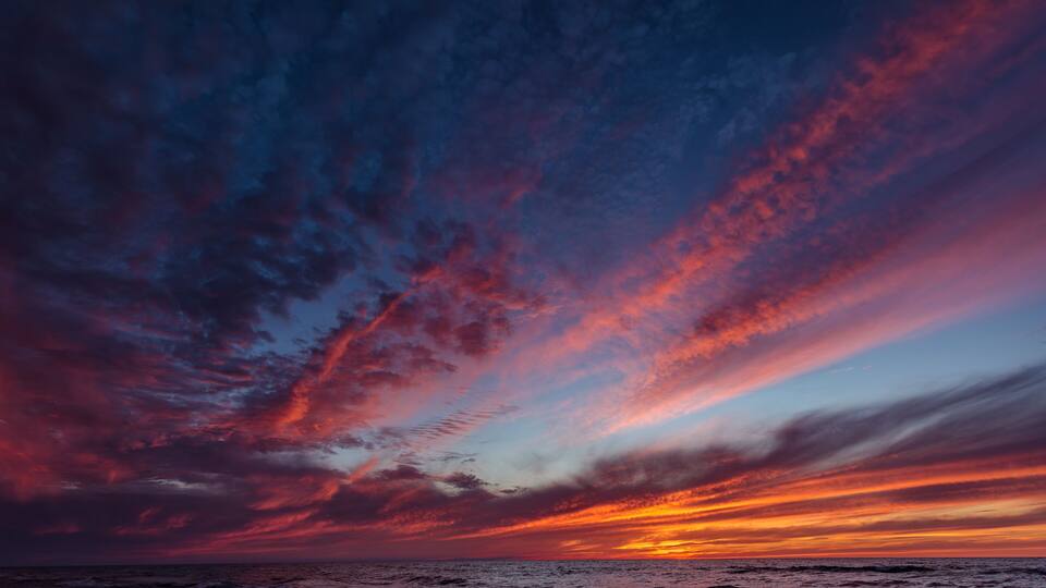 A sunset over the ocean with vibrant red and blue clouds.