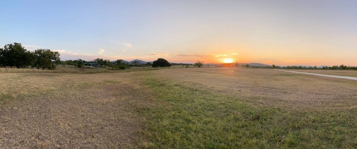 A rural landscape with a dirt path leading to a sunset.