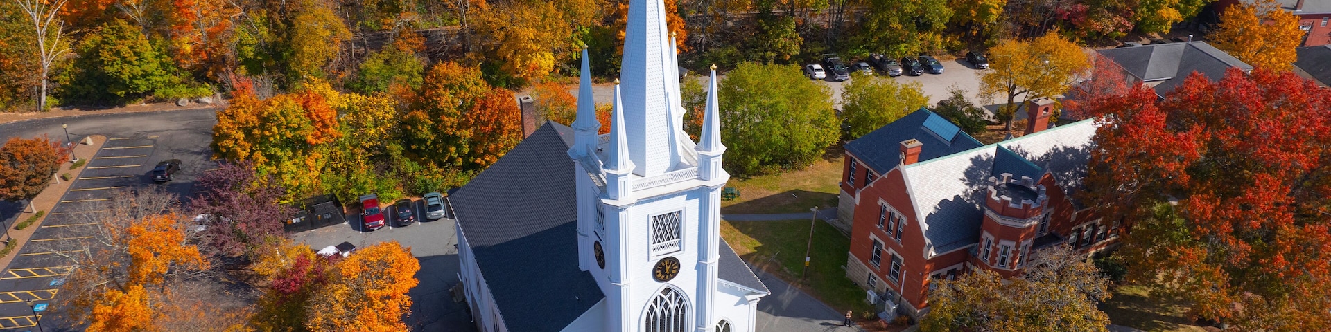 Uma igreja com uma torre alta cercada por folhagem outonal.