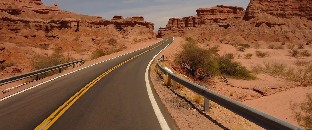 A winding road through a desert landscape with rocky cliffs on either side.