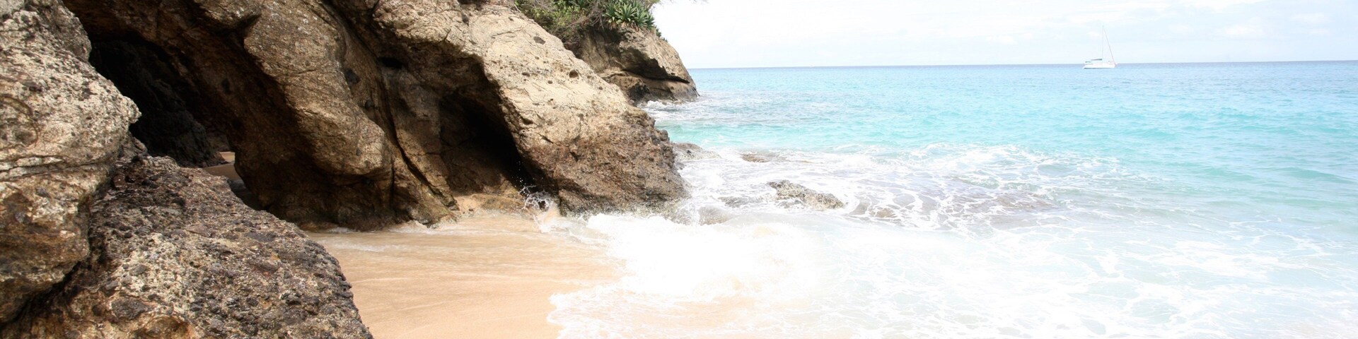 Litoral rochoso com águas turquesa cristalinas e uma praia arenosa.