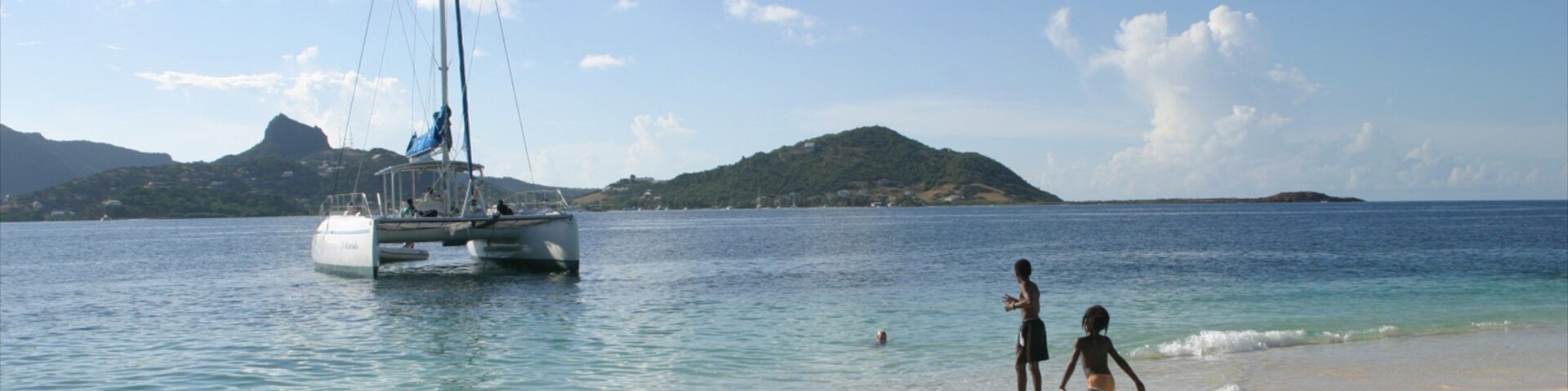 Uma praia com um veleiro, água cristalina e montanhas ao longe.