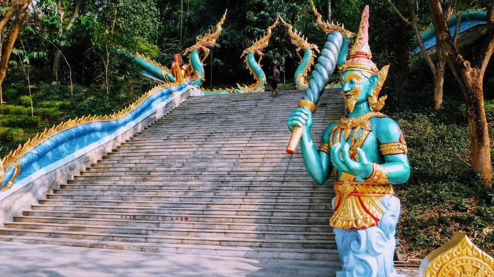 A temple staircase with a statue of a blue deity holding a staff.
