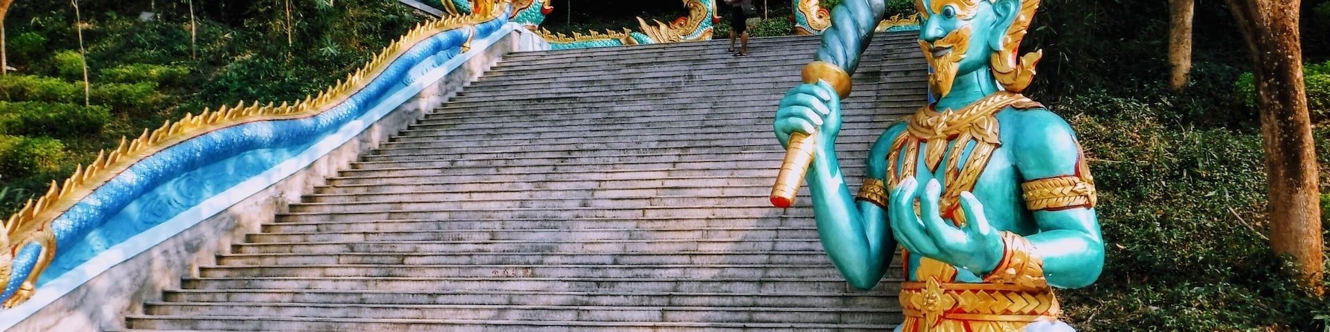 A temple staircase with a statue of a blue deity holding a staff.