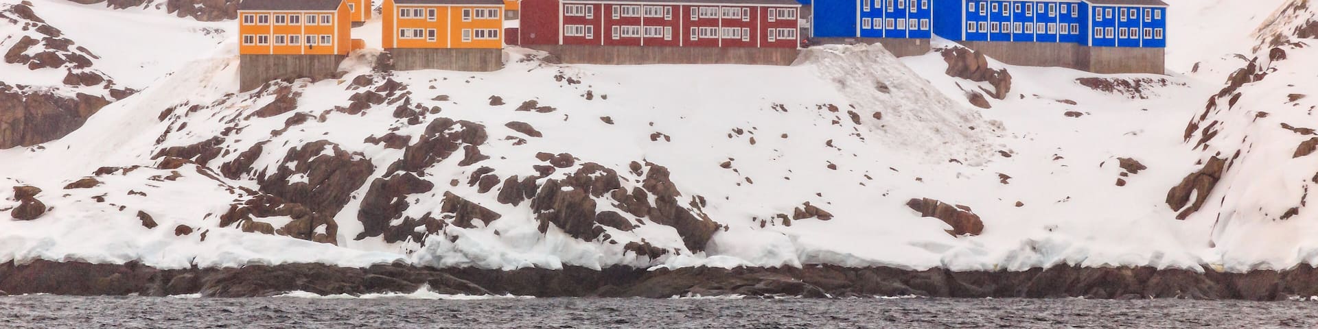 A coastal village with colorful houses on a snowy hillside.