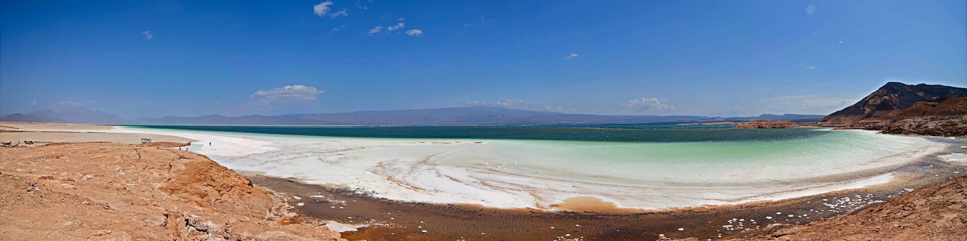 A salt flat with a turquoise lake, mountains in the background, and a clear sky.