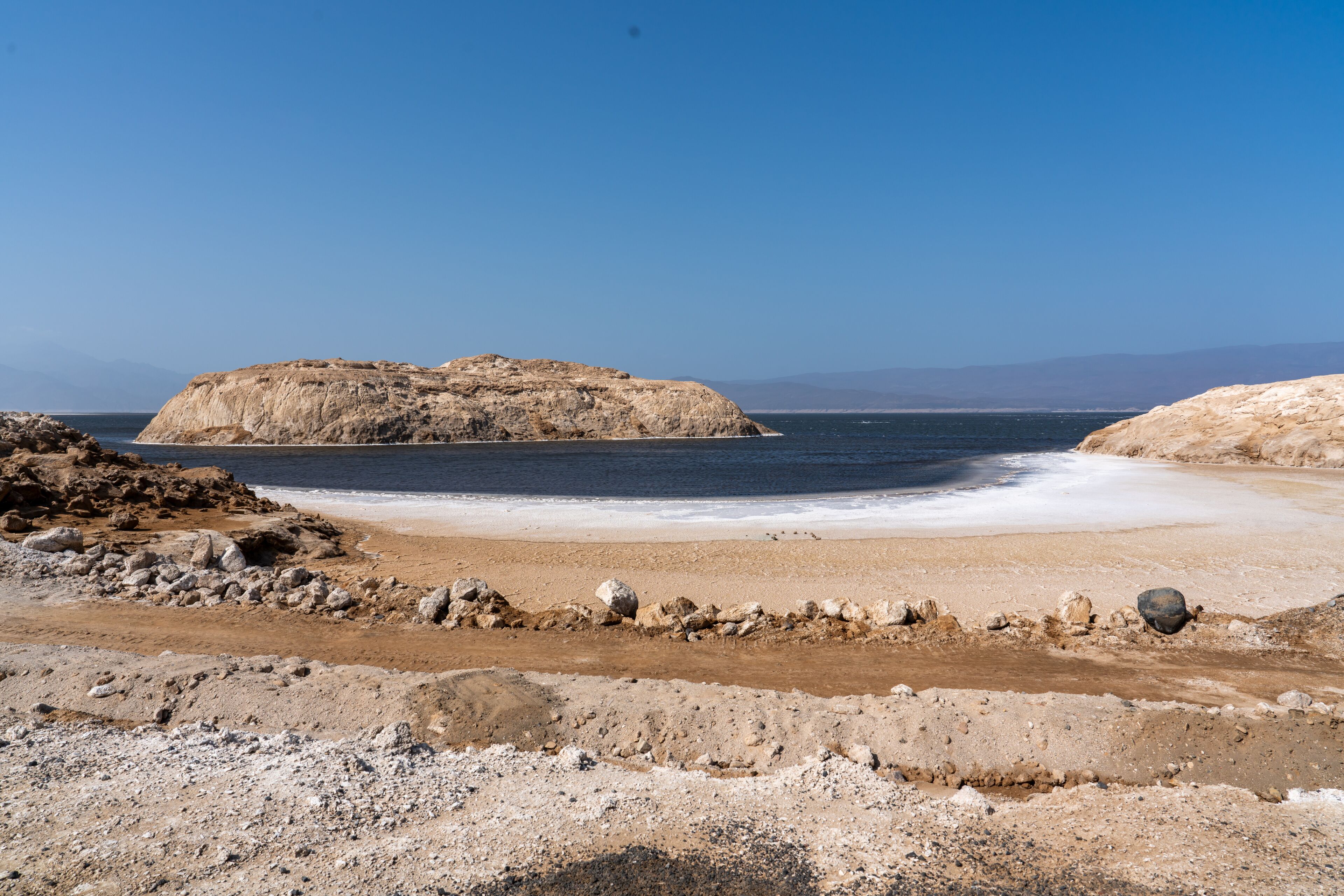 Un paisaje costero con una playa de arena, afloramientos rocosos y una gran formación rocosa a lo lejos.
