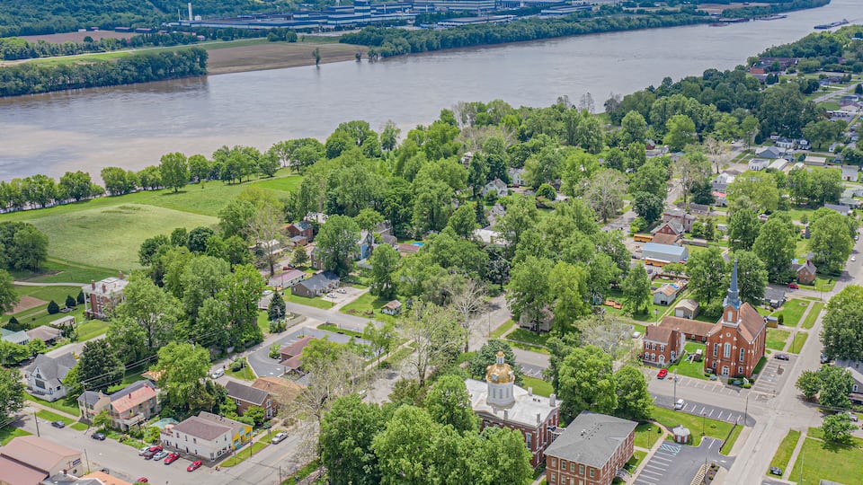 An aerial view of a town with a river, green fields, and a large building with a dome.