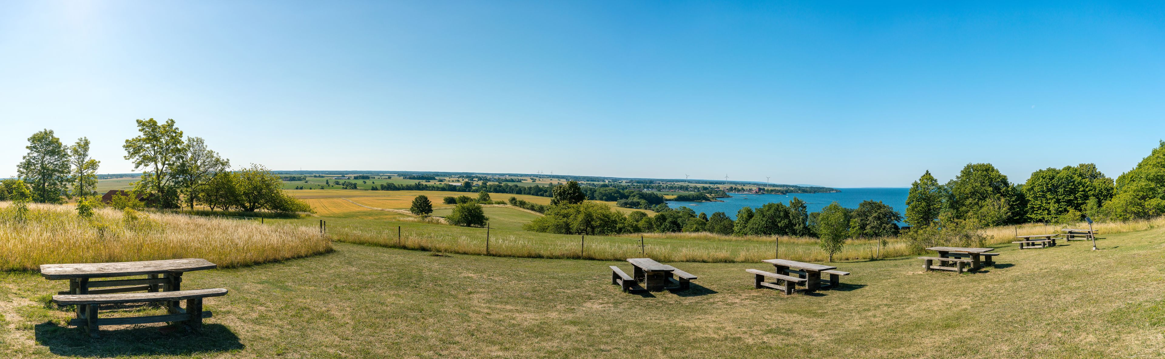 Un campo cubierto de césped con mesas de picnic y vistas a un lago y colinas distantes.