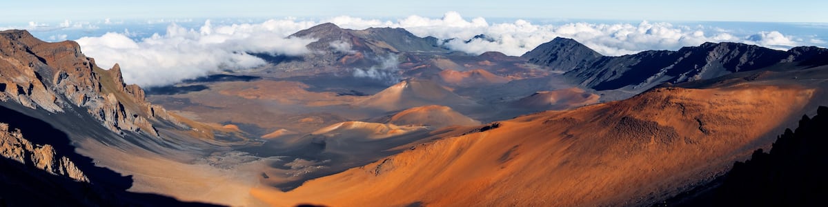 Un paysage montagneux avec une vallée et des nuages à l’horizon.