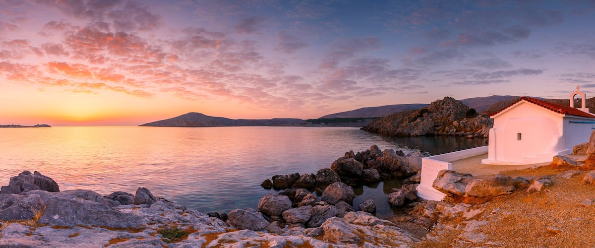 A coastal sunset with a small white church on a rocky shore.