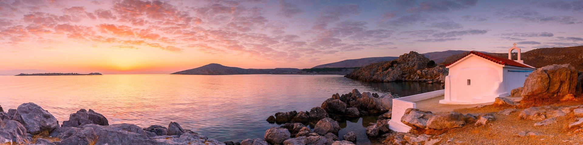 A coastal sunset with a small white church on a rocky shore.