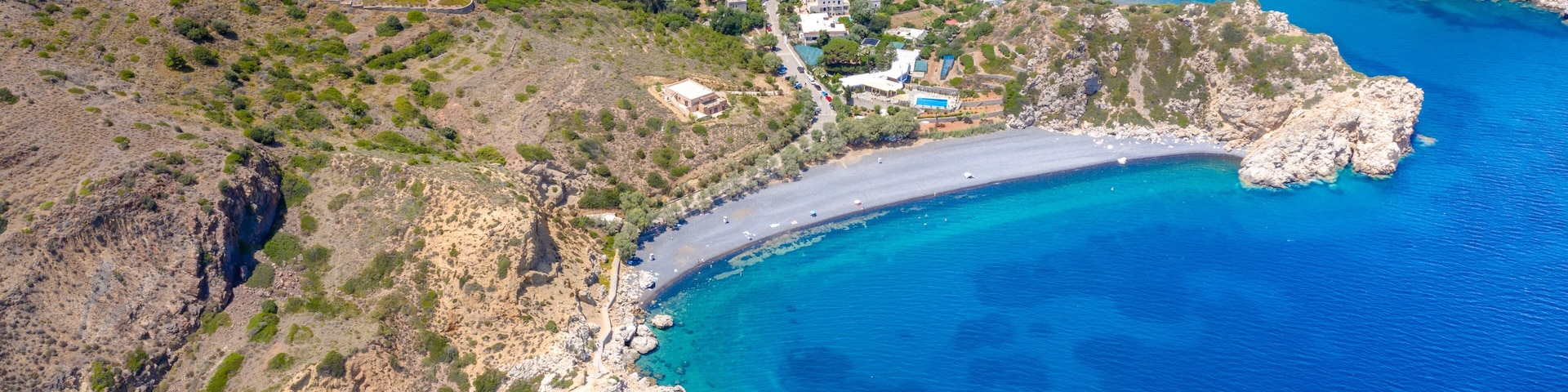 Un pueblo costero con una playa estrecha, afloramientos rocosos y aguas azules cristalinas.