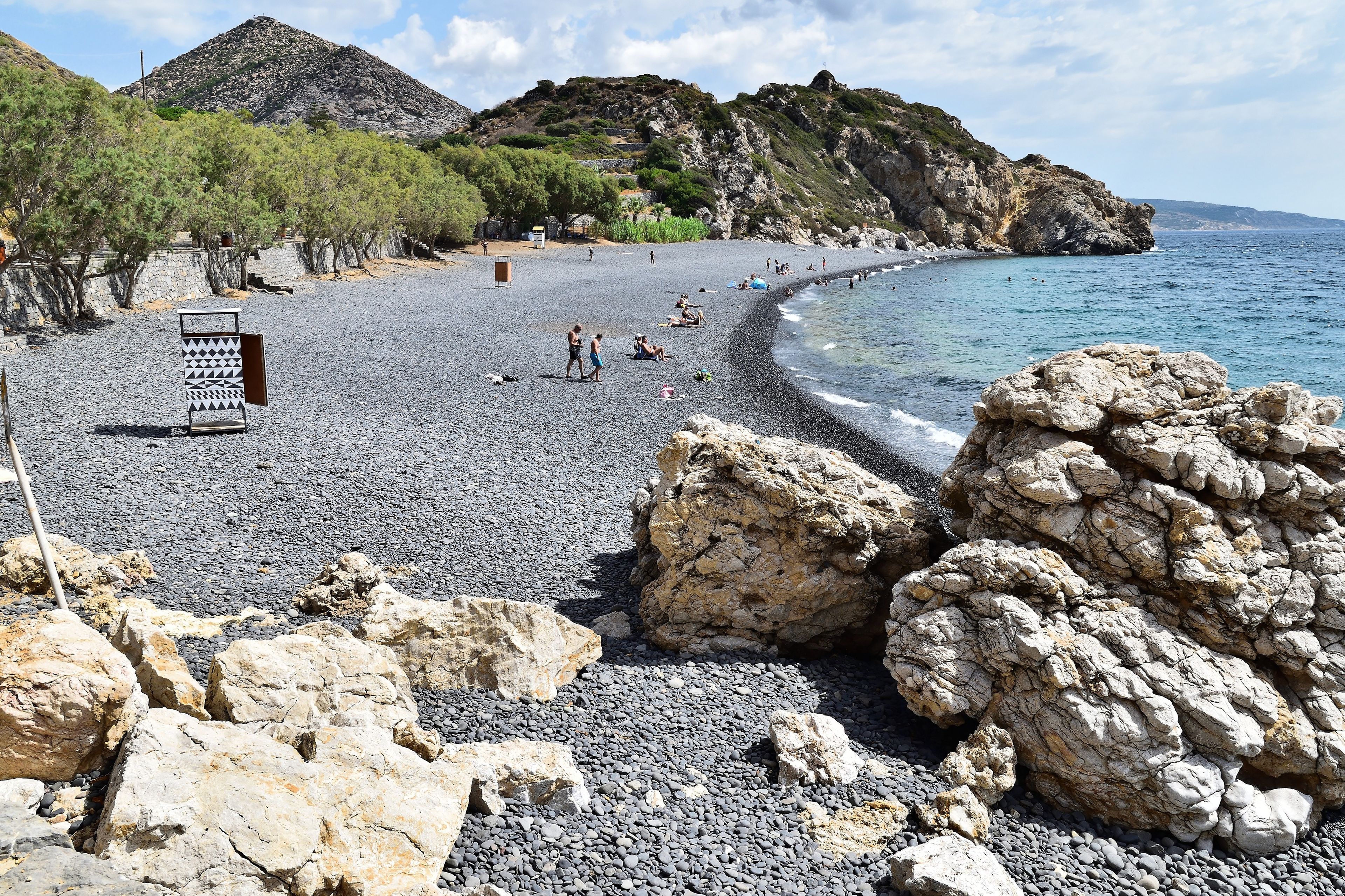 A pebble beach with rocky outcrops and a clear blue sea.