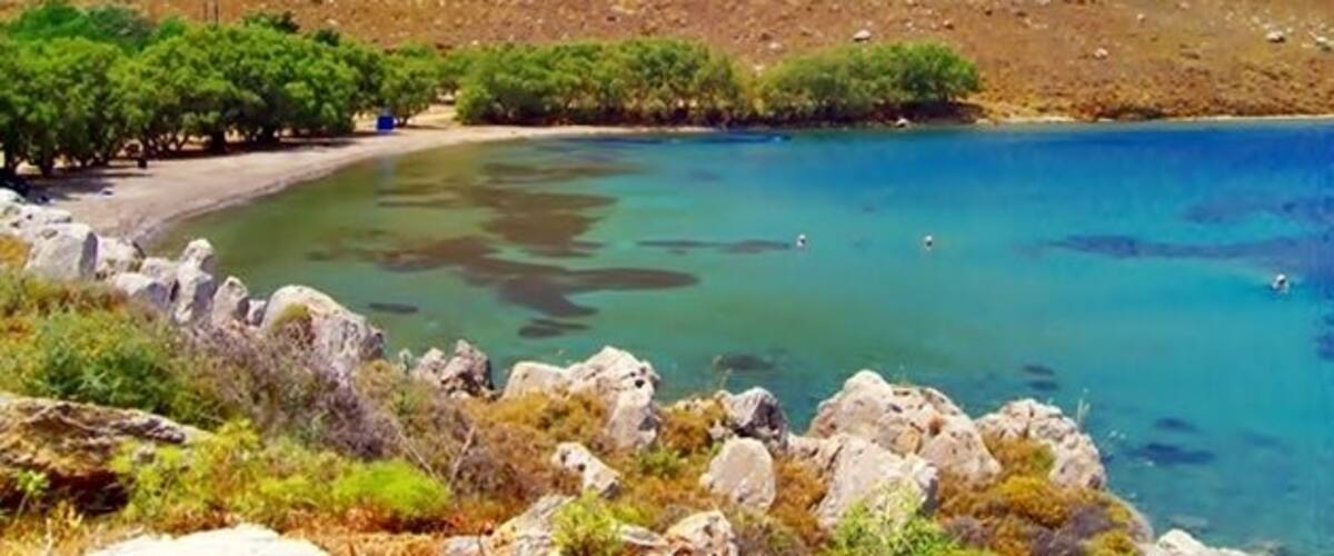 A coastal landscape with clear turquoise waters, rocky terrain, and sparse vegetation.