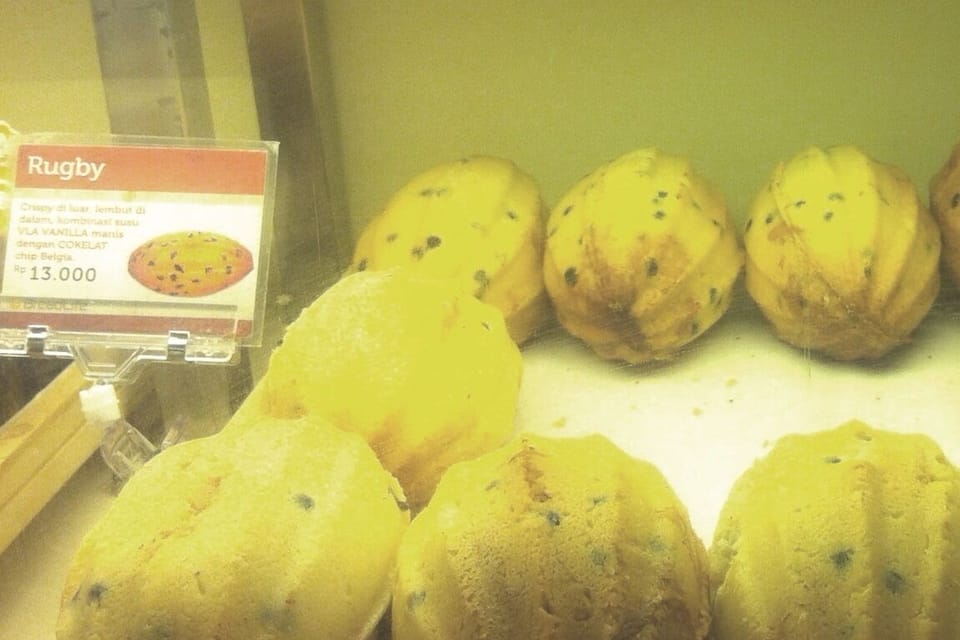 A display of yellow pastries with black specks, possibly cookies or muffins, in a bakery.