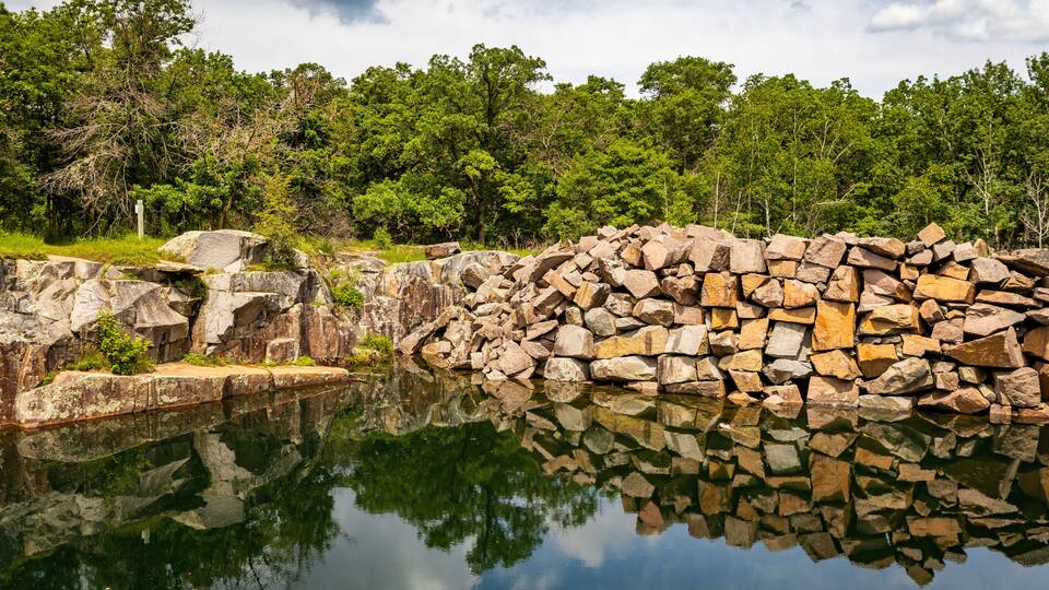 A calm lake with a rocky shoreline and dense green trees in the background.