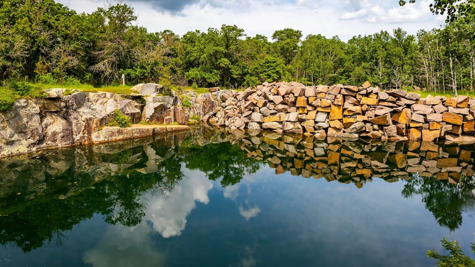 A calm lake with a stone wall and trees in the background.