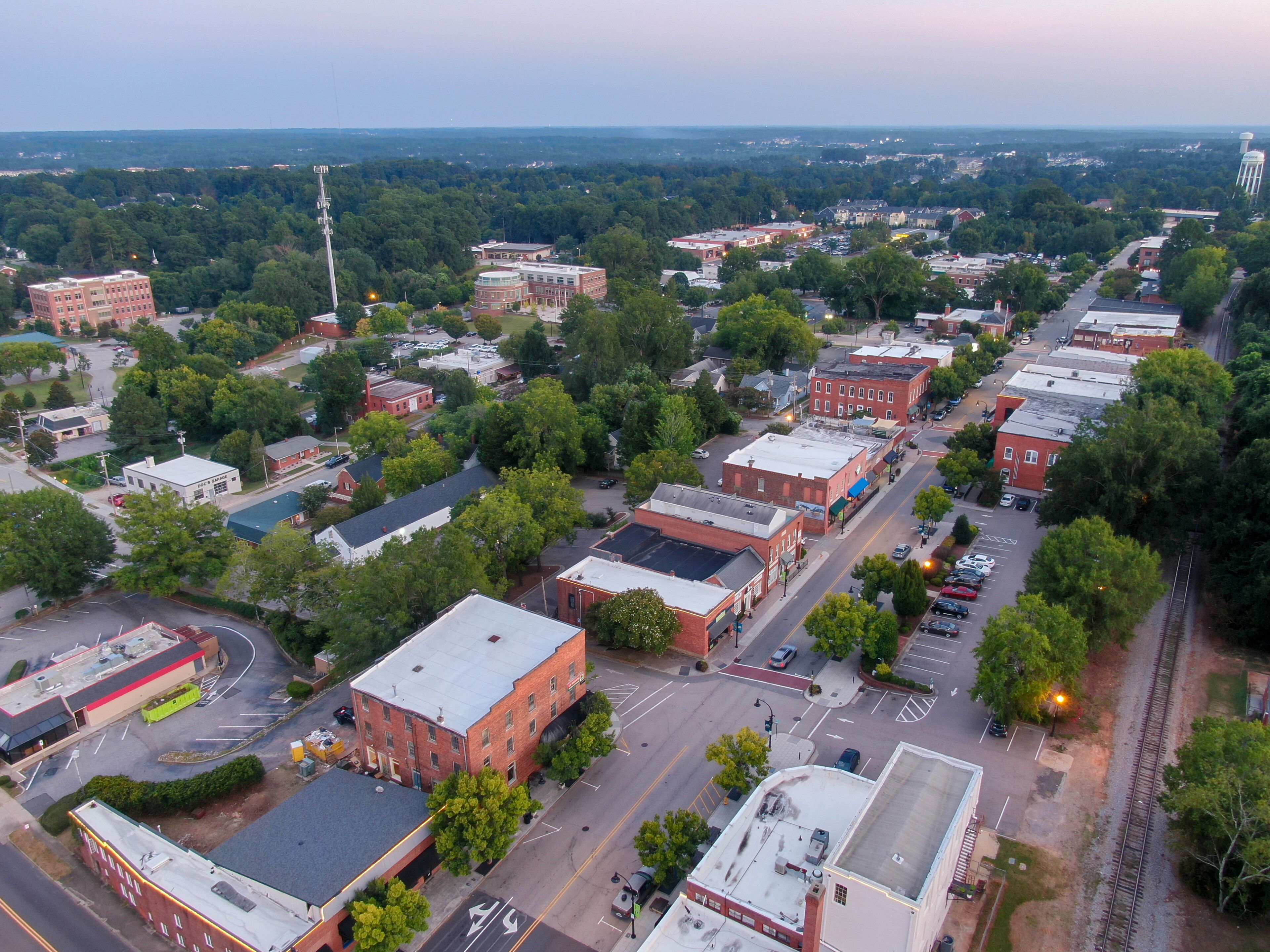 An aerial view of a town with a mix of commercial and residential buildings, a railroad track, and a large green park area.