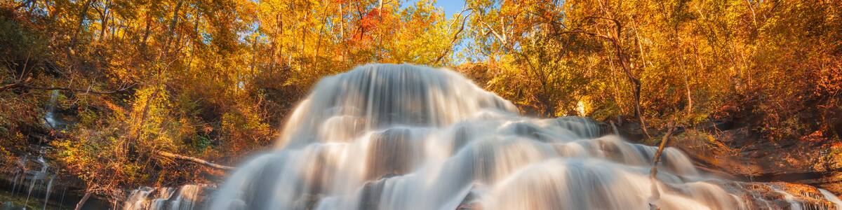 A multi-tiered waterfall surrounded by autumn-colored trees.