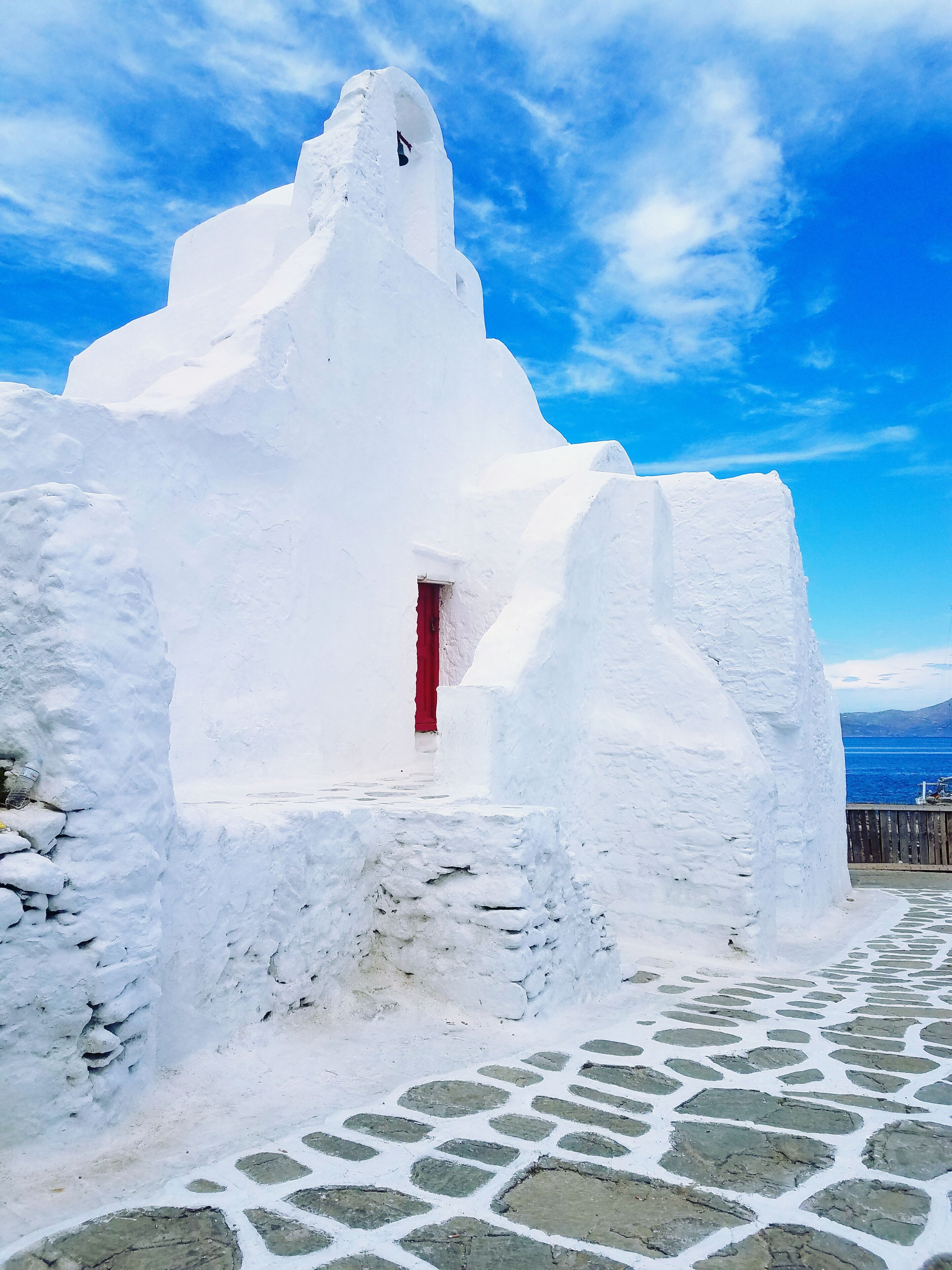 Una estructura de piedra blanca con una puerta roja, sobre un cielo azul despejado.