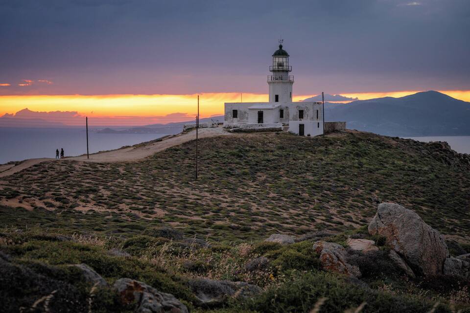 A lighthouse on a hill with a sunset in the background.