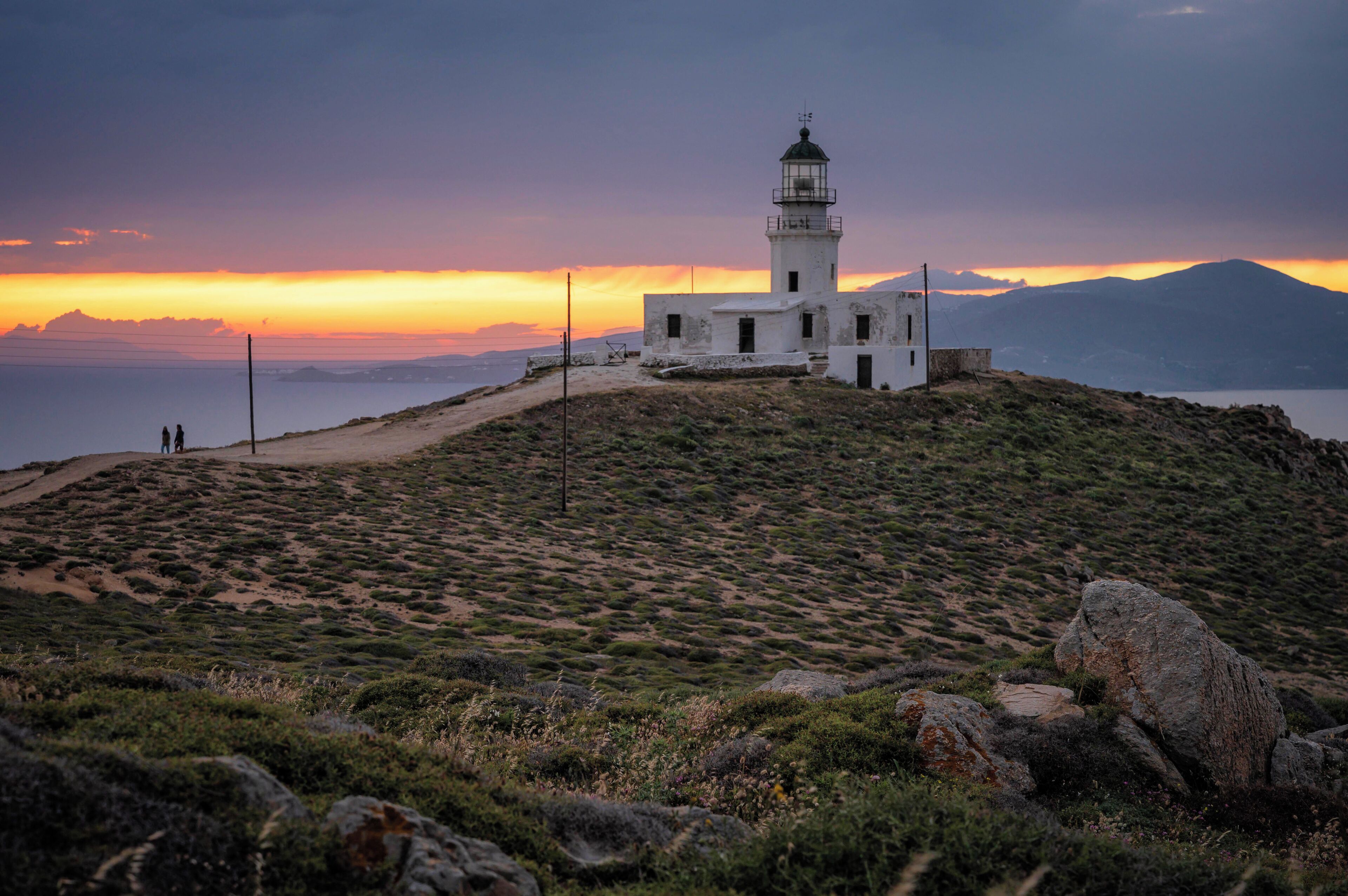 A lighthouse on a hill with a sunset in the background.