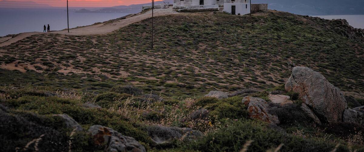 A lighthouse on a hill with a sunset in the background.