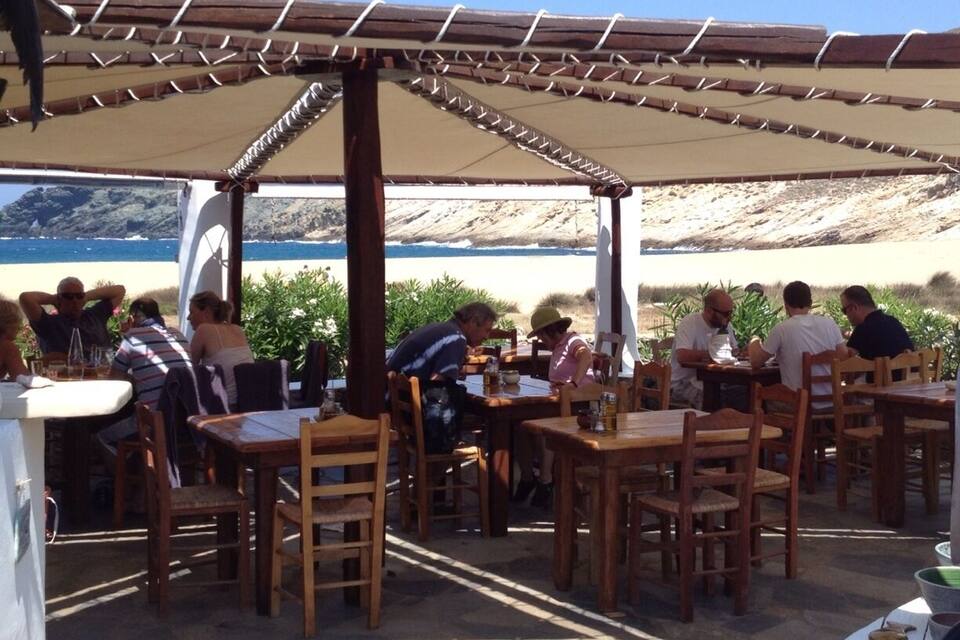 A beachside café with wooden tables and chairs, a covered seating area, and a view of the ocean.