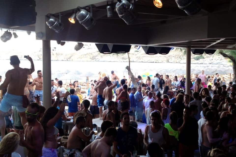 A crowded outdoor event with people gathered under a covered area with stage lights.