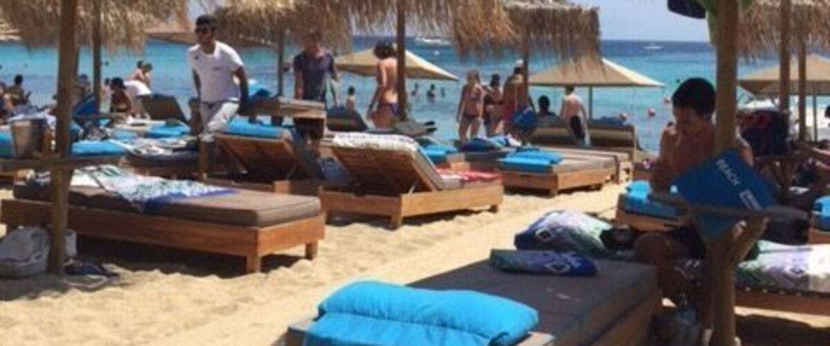 A beach with wooden lounge chairs and thatched umbrellas.