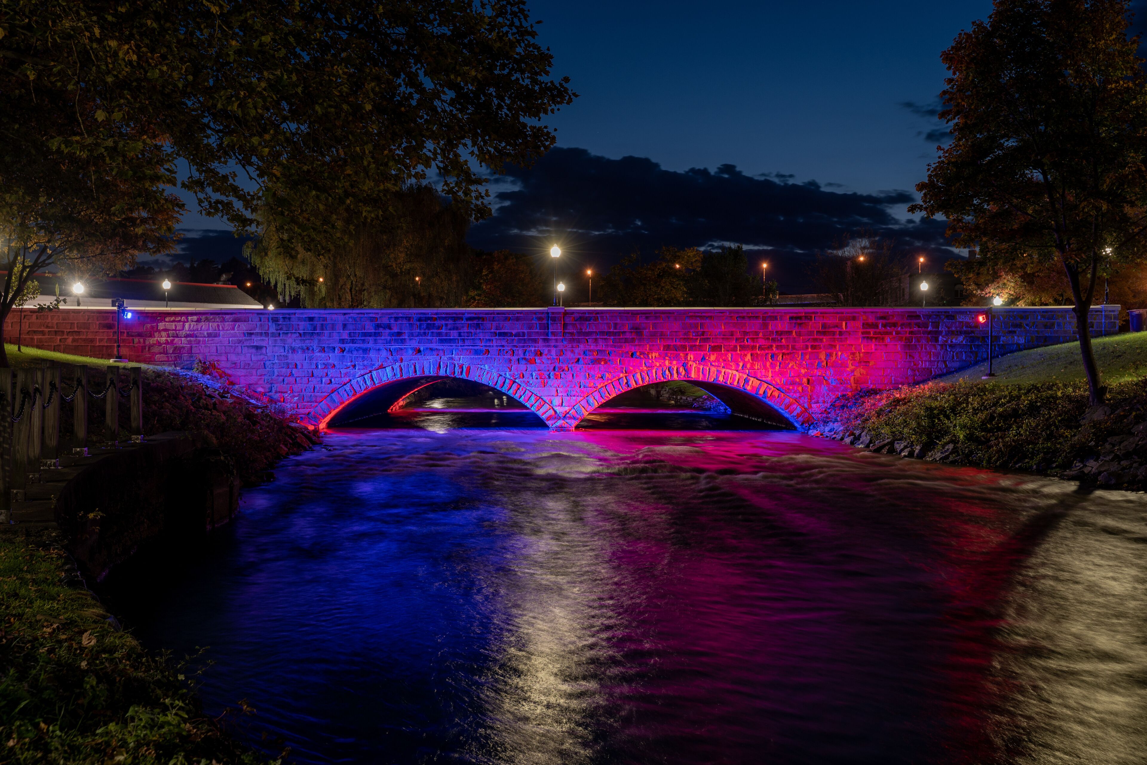 A stone bridge with arches over a river, illuminated by colorful lights.