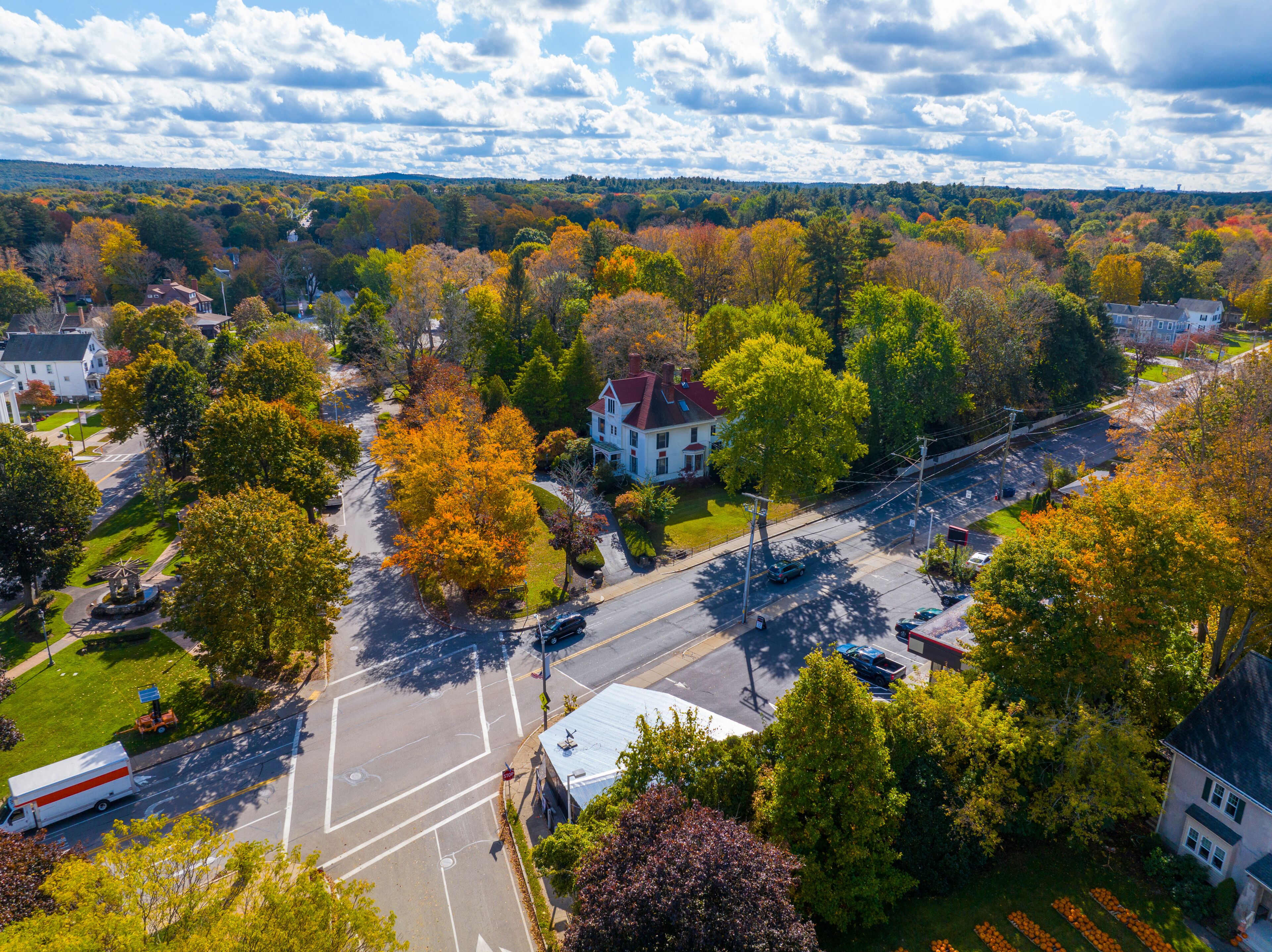 A suburban area with autumn foliage, a prominent white house with a red roof, and a clear road with vehicles.