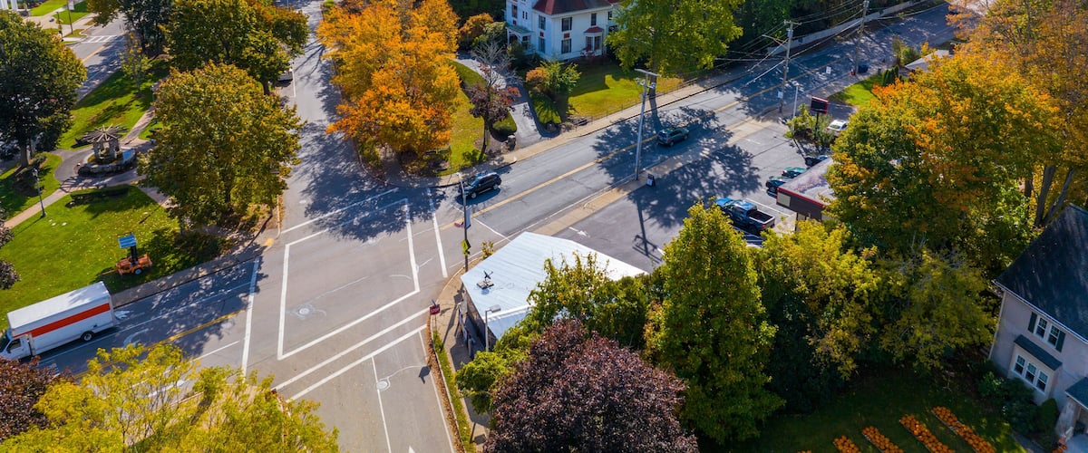 A suburban area with autumn foliage, a prominent white house with a red roof, and a clear road with vehicles.