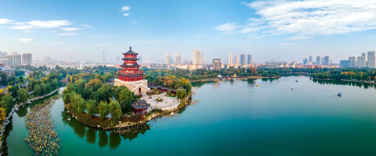 A pagoda surrounded by a lake, trees, and a city skyline.