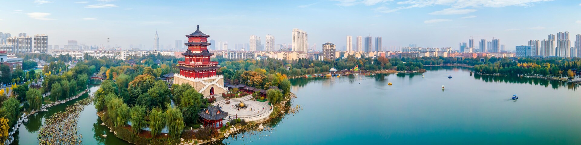 A pagoda surrounded by a lake, trees, and a city skyline.