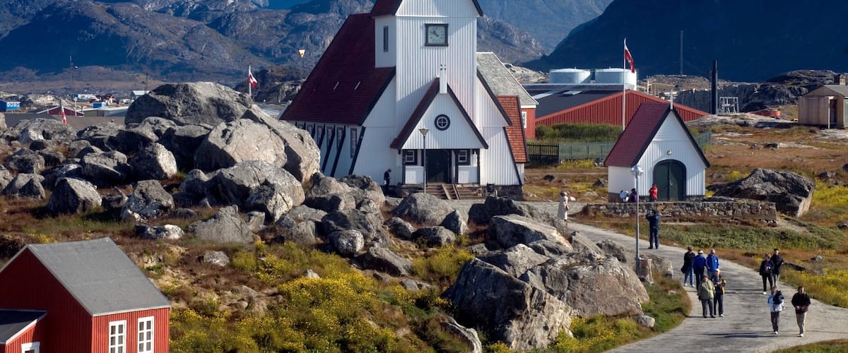 A white church with a red roof, surrounded by mountains and rocks.