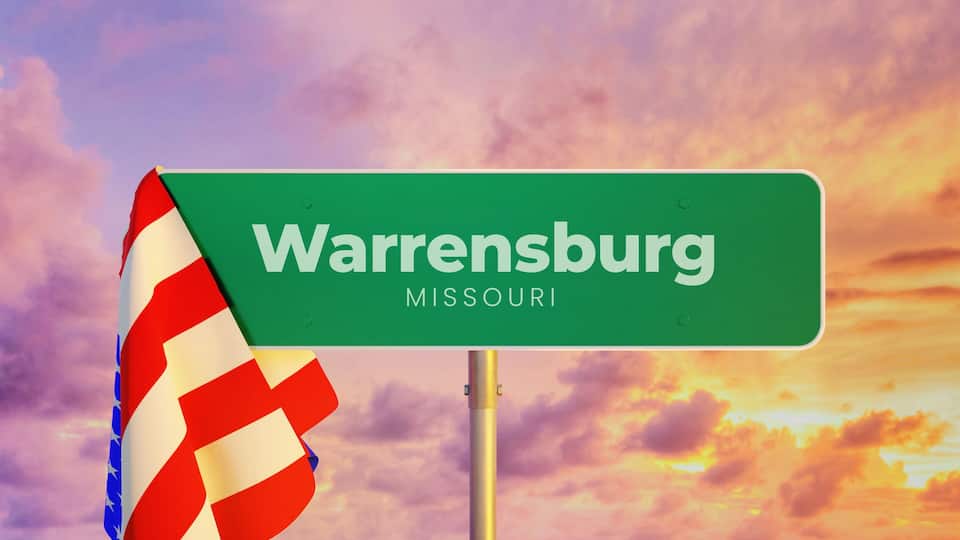 A green street sign with 'Warrensburg, Missouri' written on it, against a sunset sky.