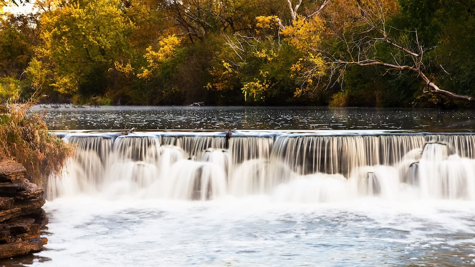 A waterfall cascading over a rocky ledge surrounded by autumn foliage.