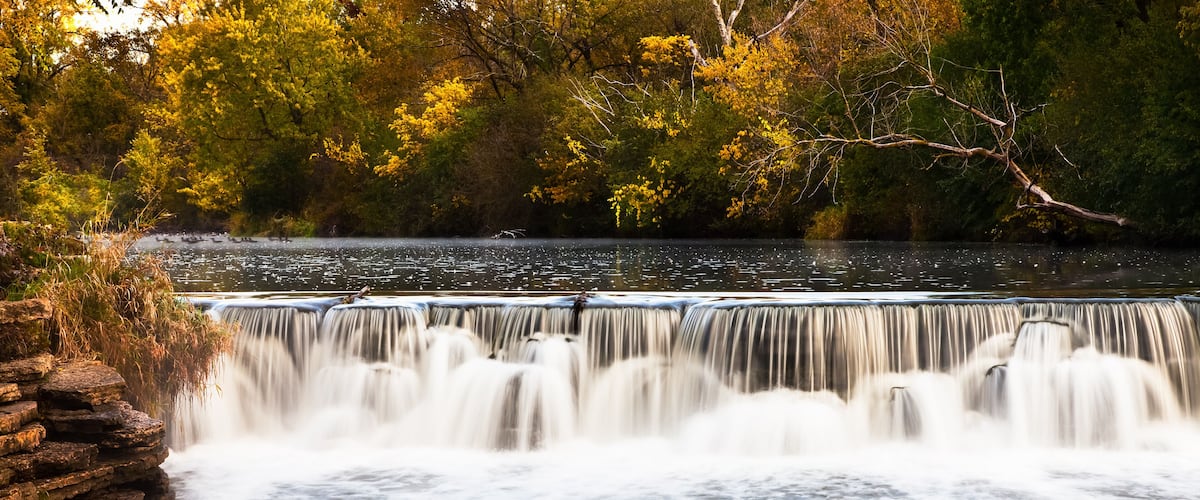 A waterfall cascading over a rocky ledge surrounded by autumn foliage.