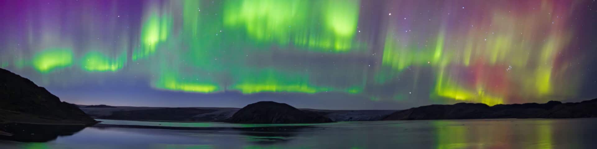 The Northern Lights over a calm lake with mountains in the background.