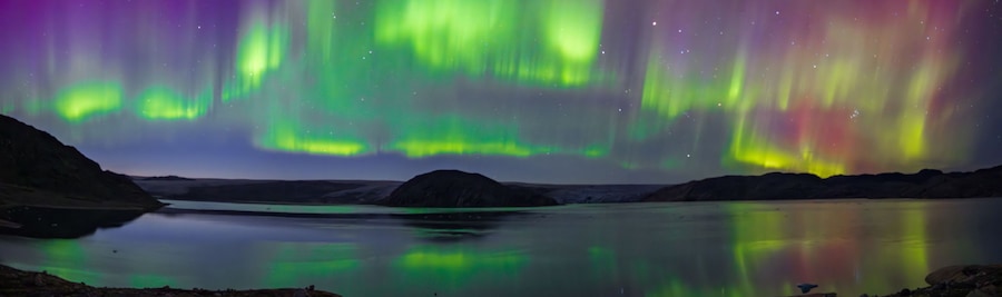 The Northern Lights over a calm lake with mountains in the background.
