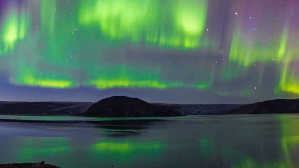 The Northern Lights over a calm lake with mountains in the background.